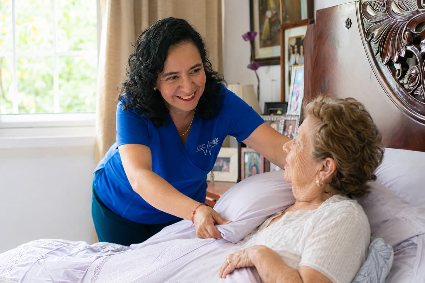 La cuidadora acomodando la almohada de una familiar mayor, ambas sonriendo